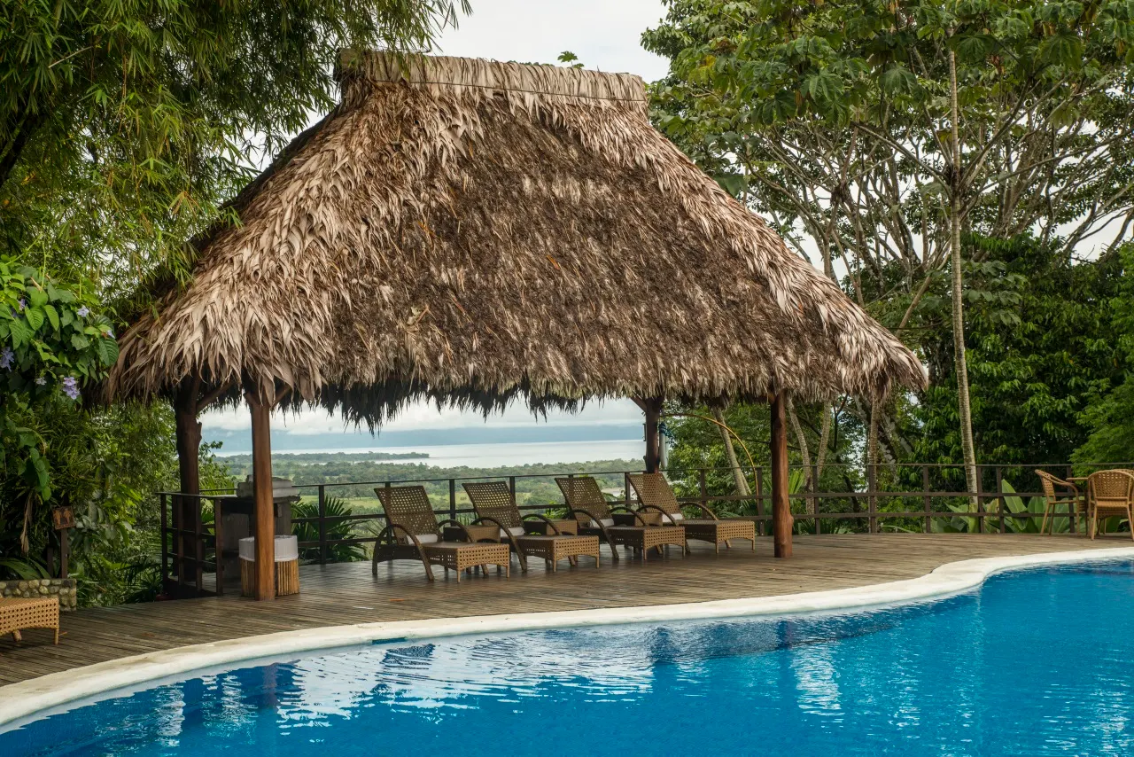 Poolbar unter großem Palmdach mit Liegen, dahinter Blick auf den Golfo Dulce