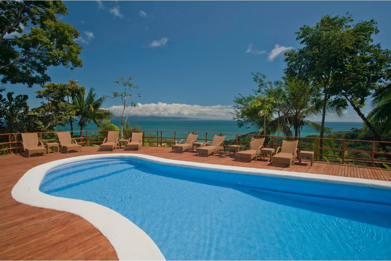 Blauer Pool mit Holzdeck und Liegen über der Pazifikküste in der Lapa Rios Lodge