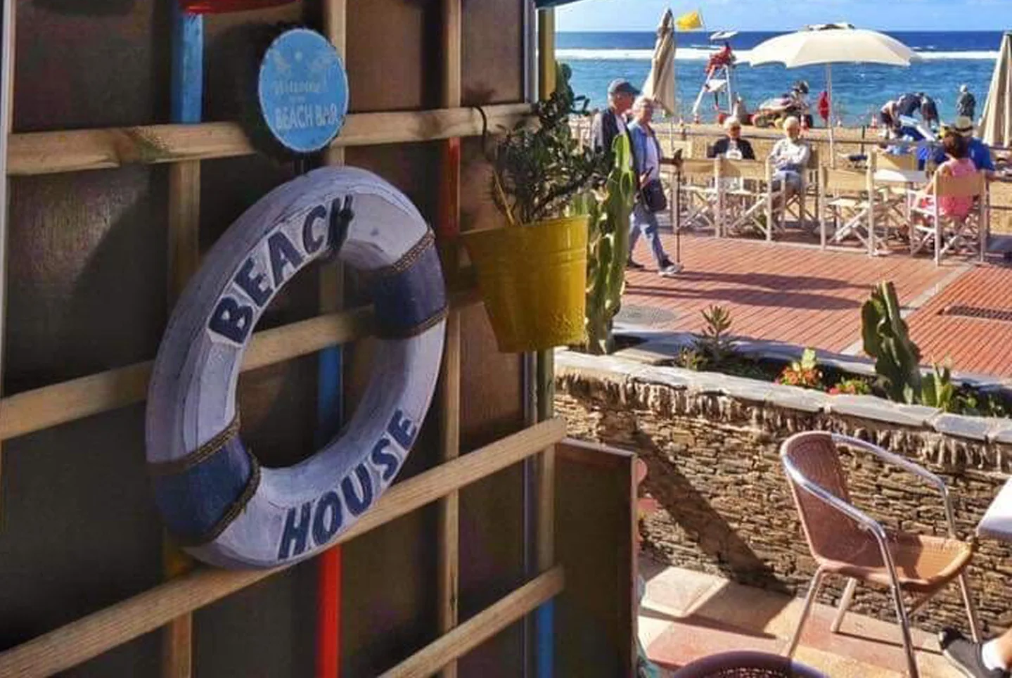 Terrasse des The Couple an der Promenade Las Canteras, Rettungsring mit Aufschrift Beach House an der Wand, dahinter der Strand