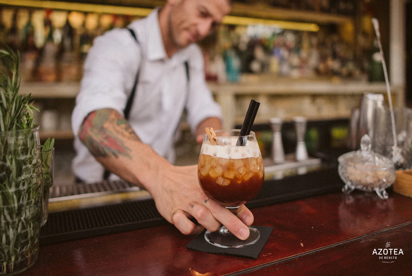 Barkeeper reicht einen Cocktail mit Zimtstange über den Holztresen der Azotea de Benito