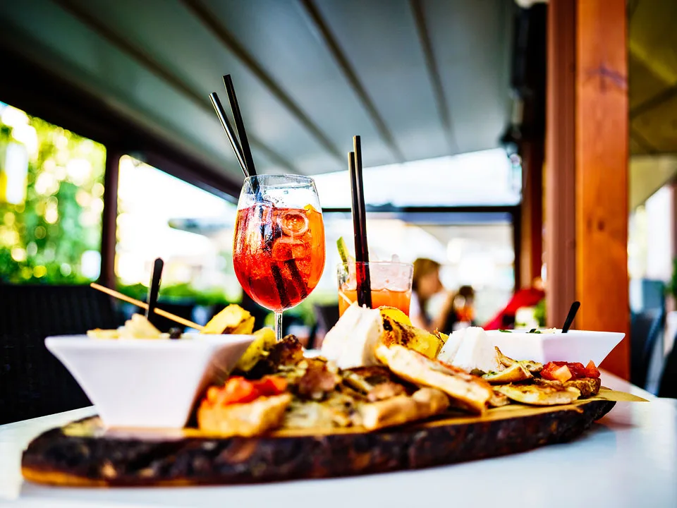 Holzbrett mit Bruschetta und Käse vor einem Aperitif-Glas auf einer Barterrasse