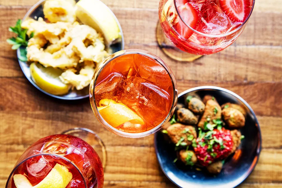 Aperitif-Gläser auf einem Holztisch, daneben Schälchen mit frittiertem Tintenfisch und Oliven