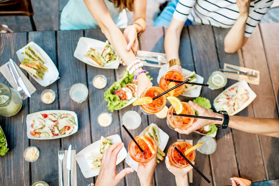 Vier Hände stoßen über einem Tisch mit Aperol Spritz und belegten Häppchen an