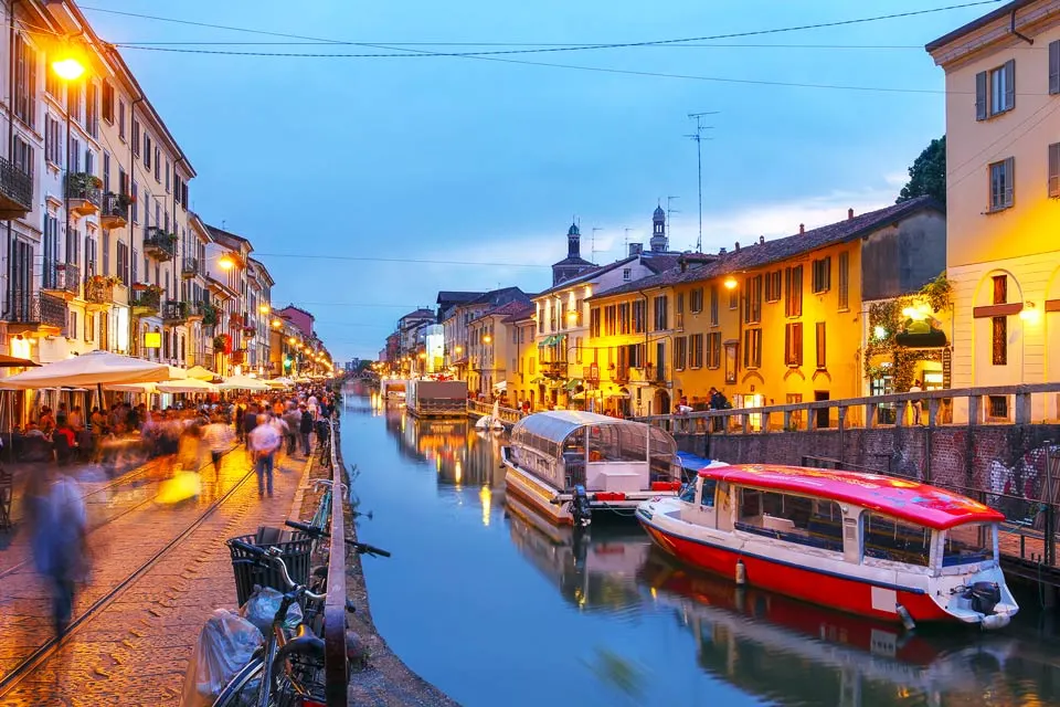Beleuchtete Kanalpromenade der Navigli in der Dämmerung mit Booten und vielen Spaziergängern