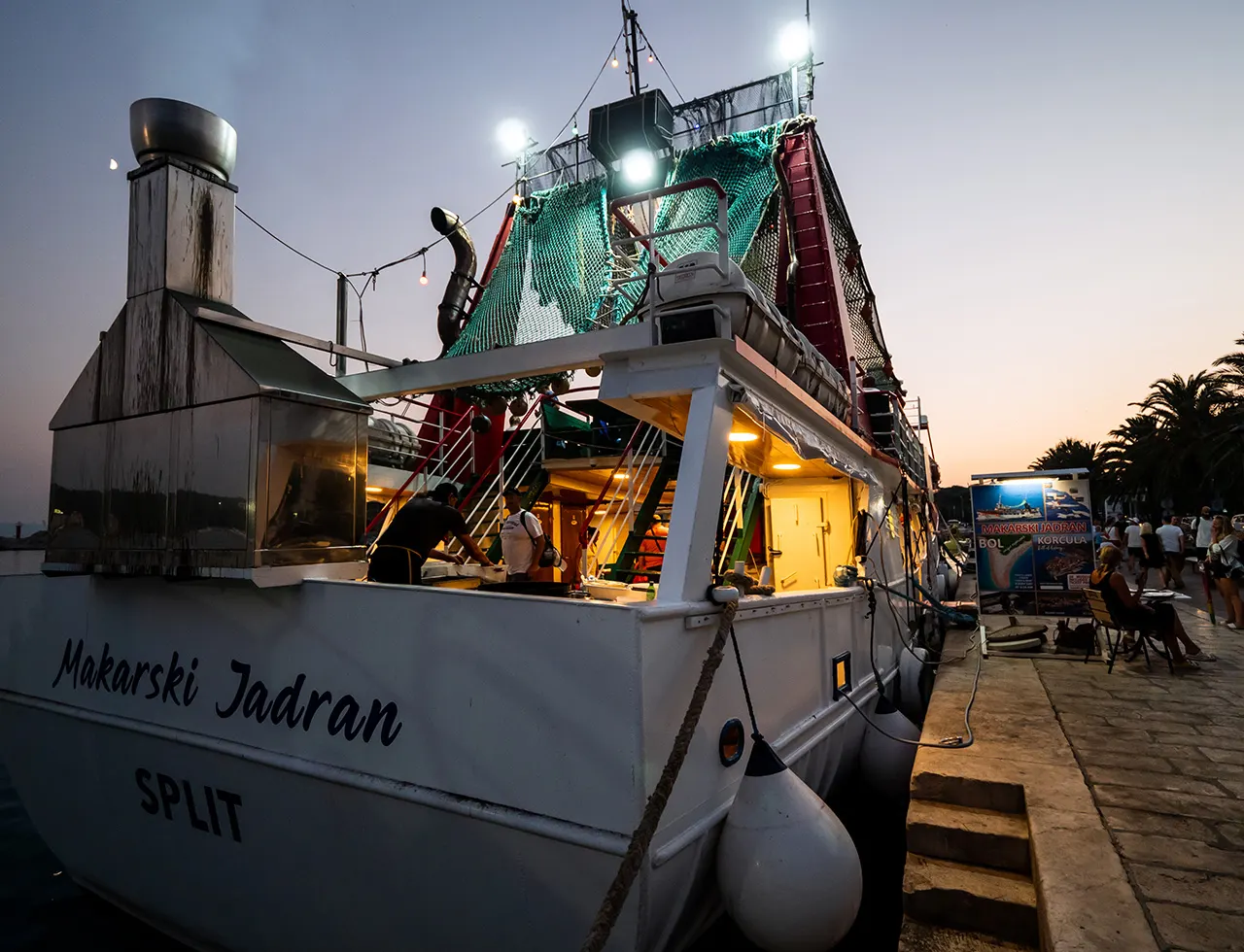 Fischkutter Makarski Jadran am Hafenkai in der Dämmerung, Crew bereitet den Verkauf vor