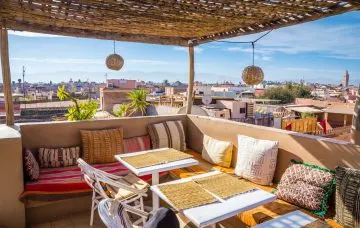 Dachterrasse mit Bastdach, Korblampen und Kissenbank über den Dächern von Marrakesch