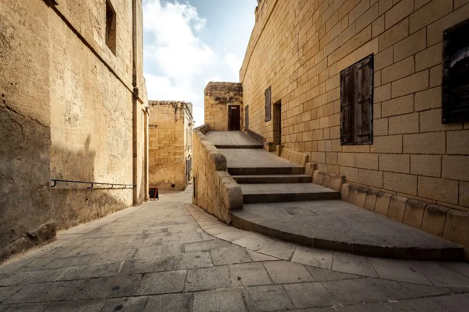 Gepflasterte Gasse mit breiter Steintreppe zwischen hohen Kalksteinmauern unter Wolkenhimmel