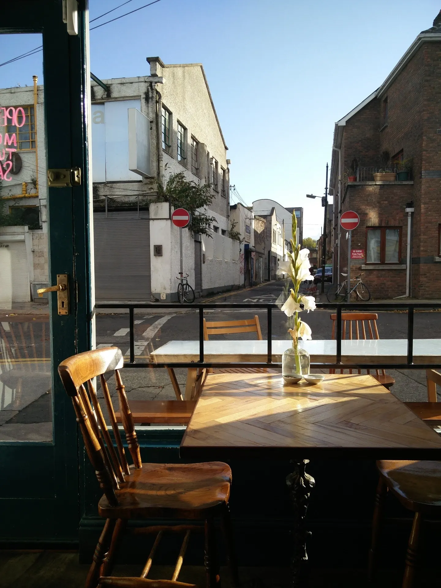 Blick vom Fenstertisch durch grüne Tür auf leere Straße, Gladiolen in einer Vase