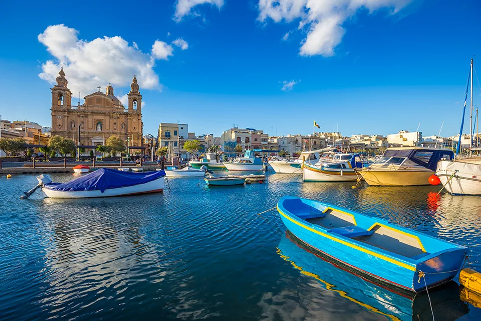 Bunte Boote im Hafenbecken von Msida, dahinter die Pfarrkirche mit ihren Türmen