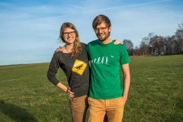 Frau und Mann stehen Arm in Arm auf einer Wiese und lächeln in die Kamera