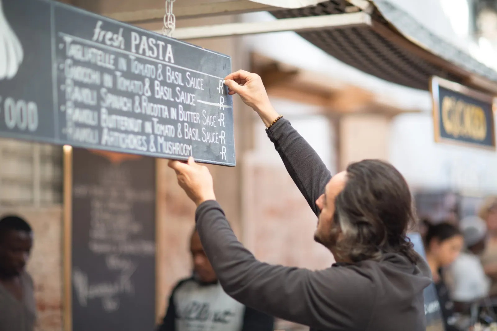 Mann hängt eine Kreidetafel mit der Pasta-Karte über einem Marktstand auf
