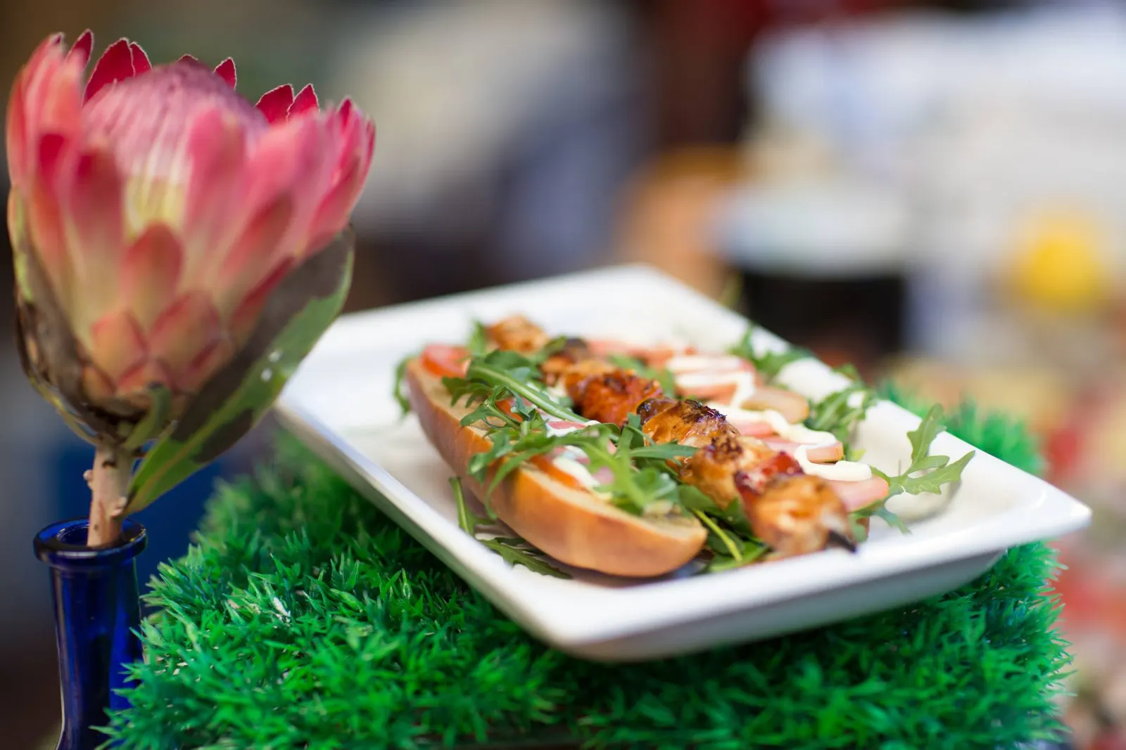 Baguette mit Garnelen und Rucola auf weißem Teller, daneben eine Protea-Blüte