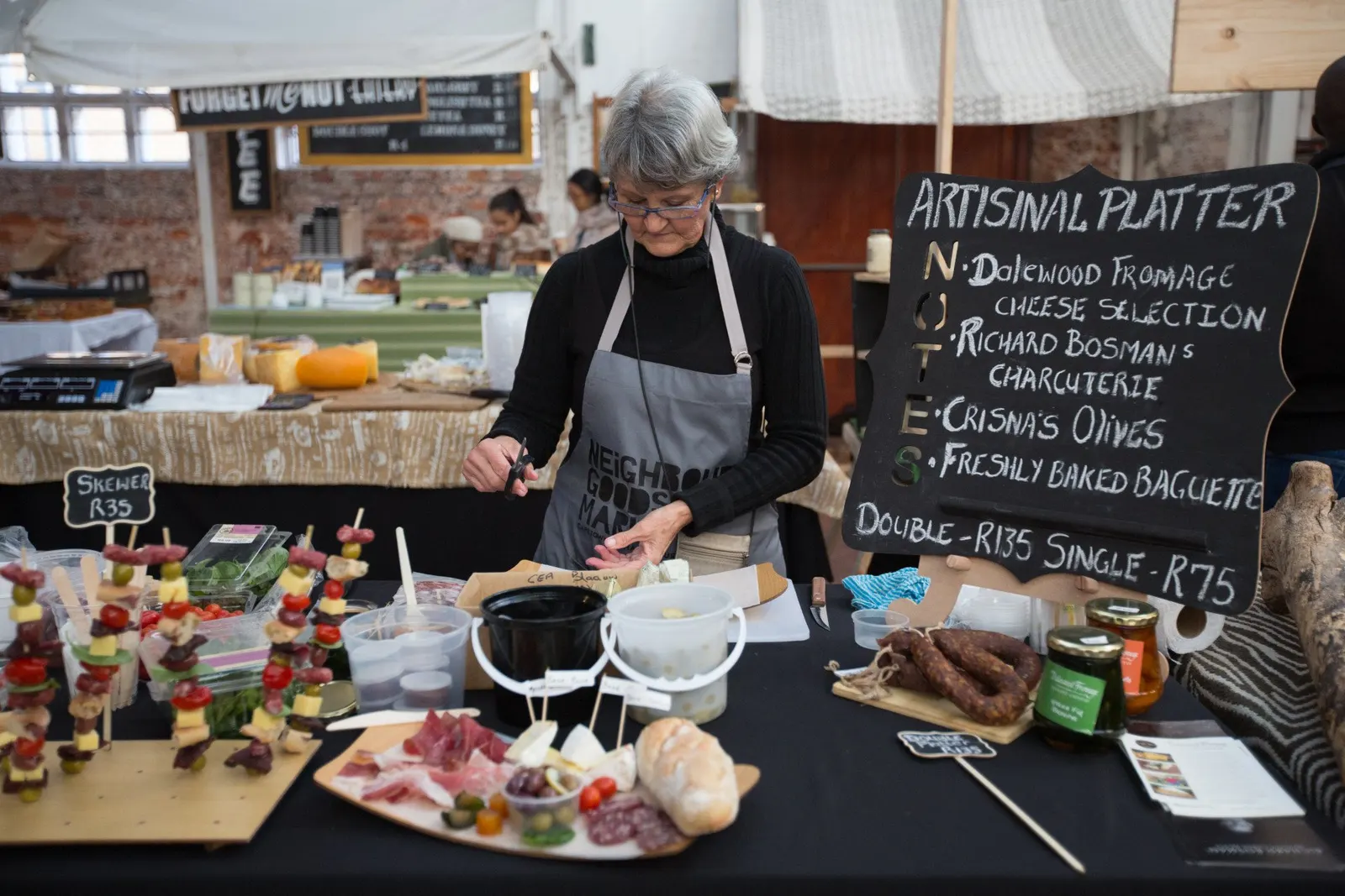 Verkäuferin richtet eine Wurst- und Käseplatte an, Tafel mit Aufschrift „Artisinal Platter“
