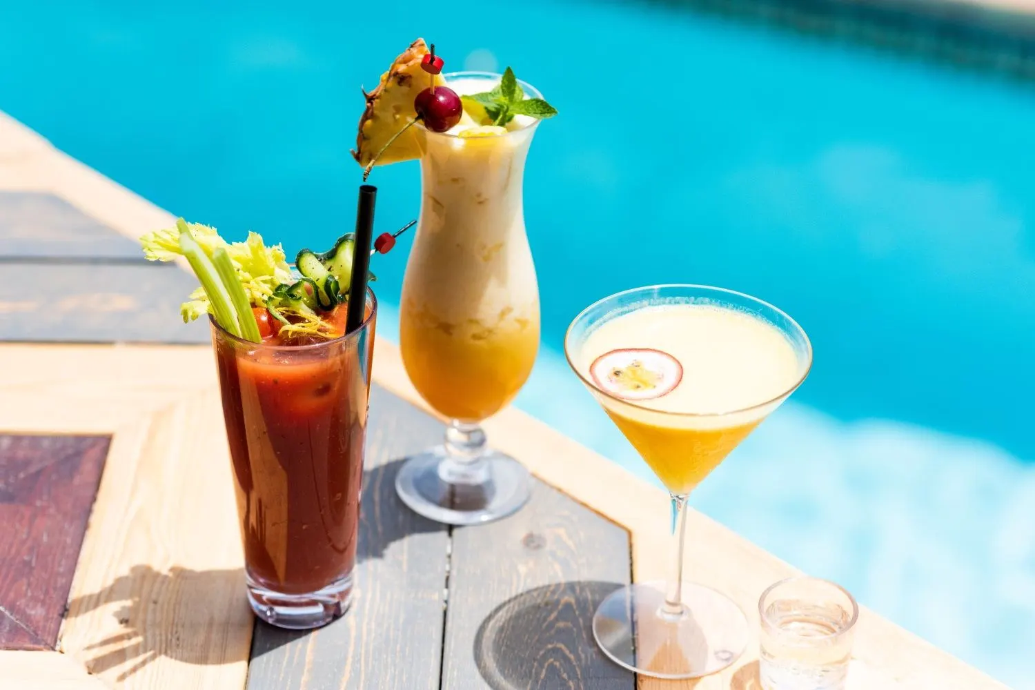 Drei Cocktails auf einem Holzsteg direkt am blauen Poolwasser