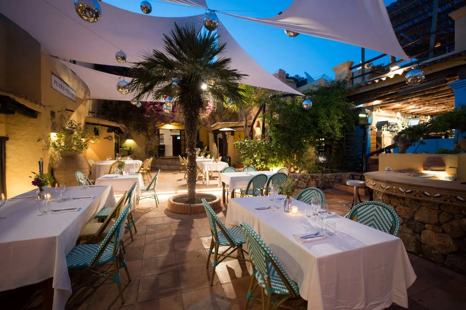 Restaurantterrasse in der Abenddämmerung mit türkisen Bistrostühlen rund um eine Palme