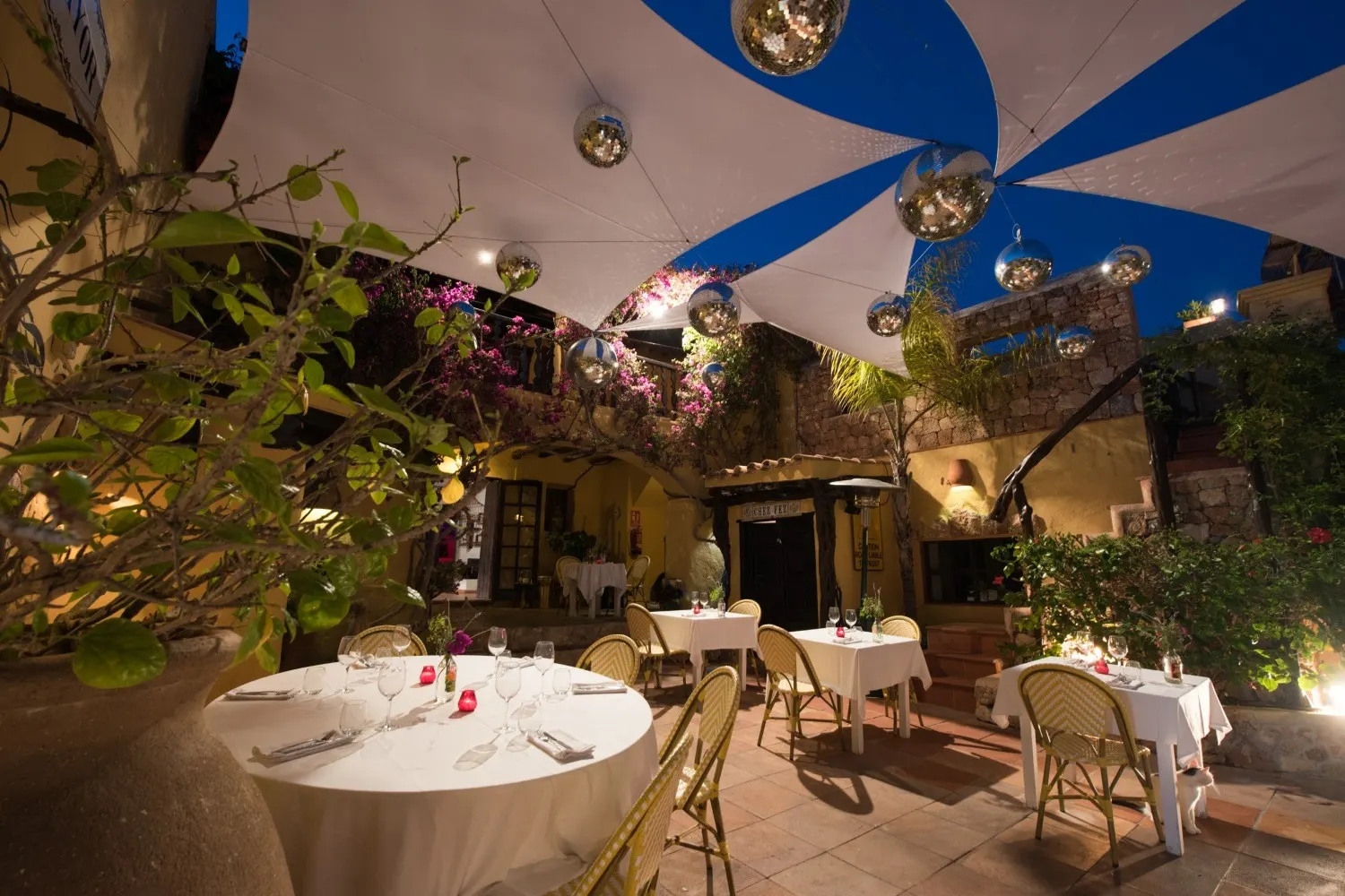 Gedeckte Restauranttische im Innenhof am Abend unter blau-weißen Sonnensegeln und Discokugeln