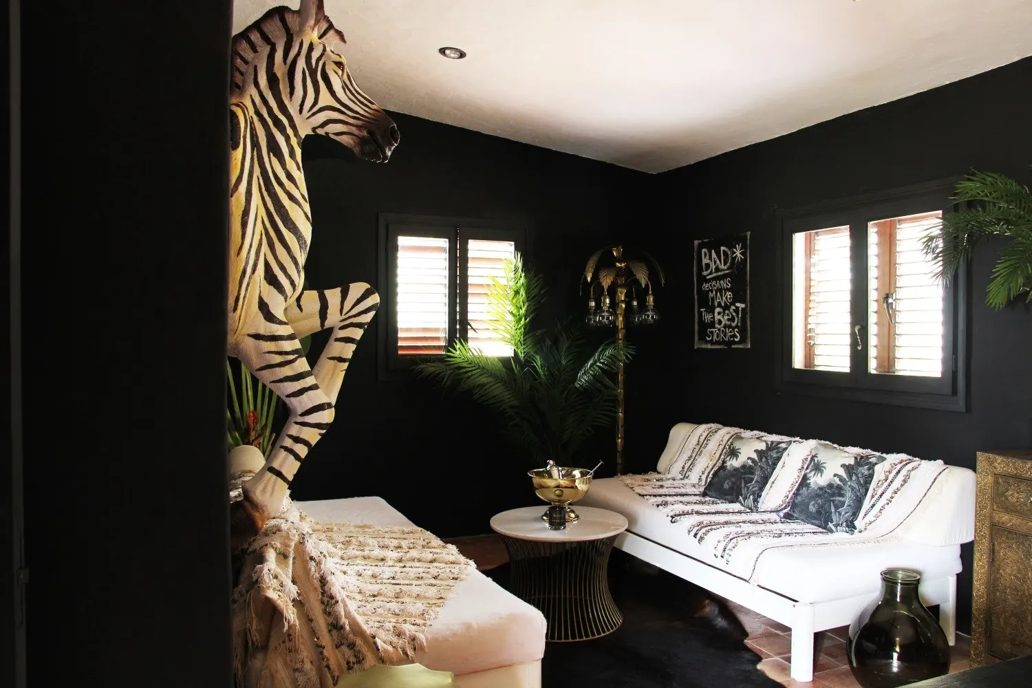 Schwarz gestrichener Raum mit weißen Sitzbänken, Zimmerpalme und einer Zebra-Skulptur an der Wand