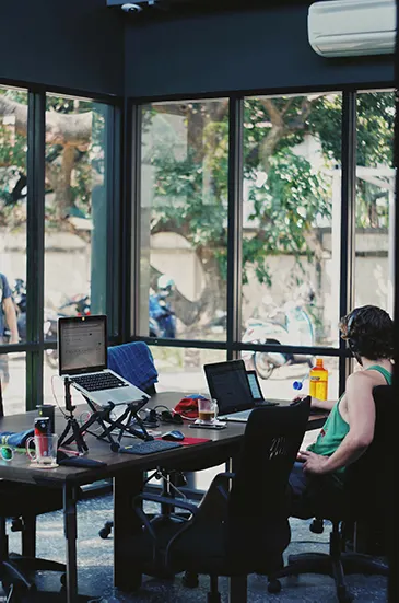 Coworking-Ecke mit Laptopständer und Gläsern an der Fensterfront, draußen parkende Motorroller