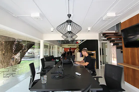 Coworking-Raum mit langem schwarzem Tisch, Mann am Laptop und Drahtkorbleuchten