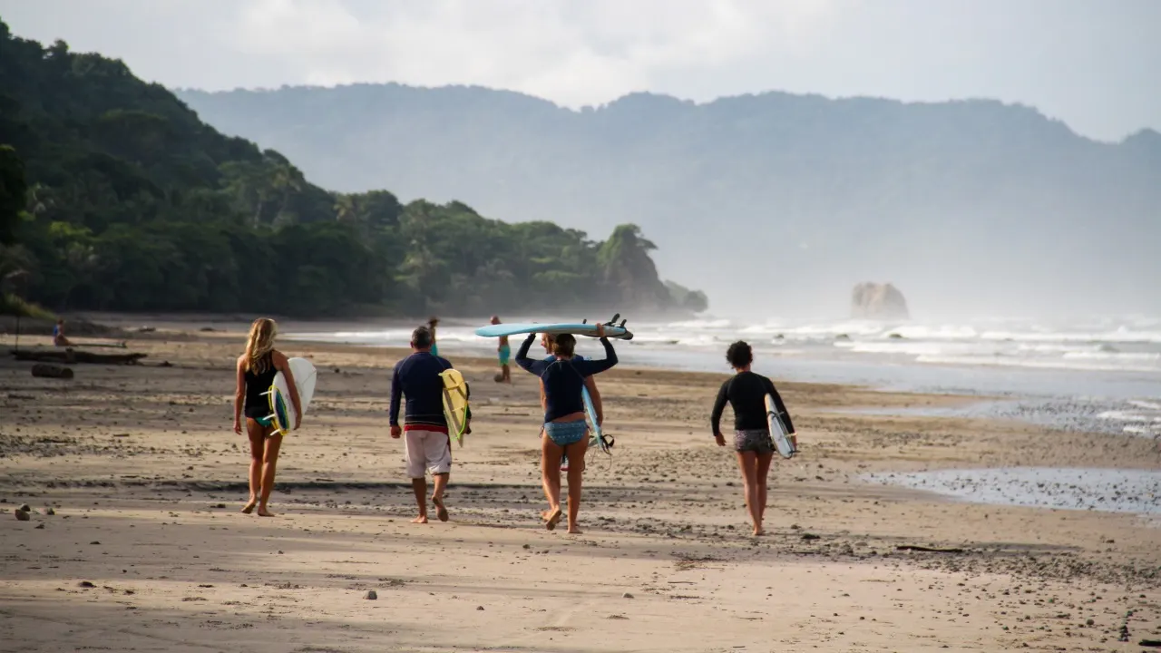 Vier Surferinnen und ein Surfer tragen ihre Bretter über den Strand zur Brandung