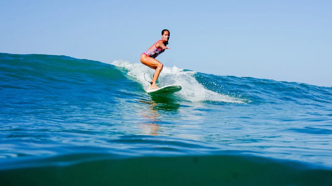 Surferin im pinken Badeanzug reitet eine flache Welle auf dem Longboard