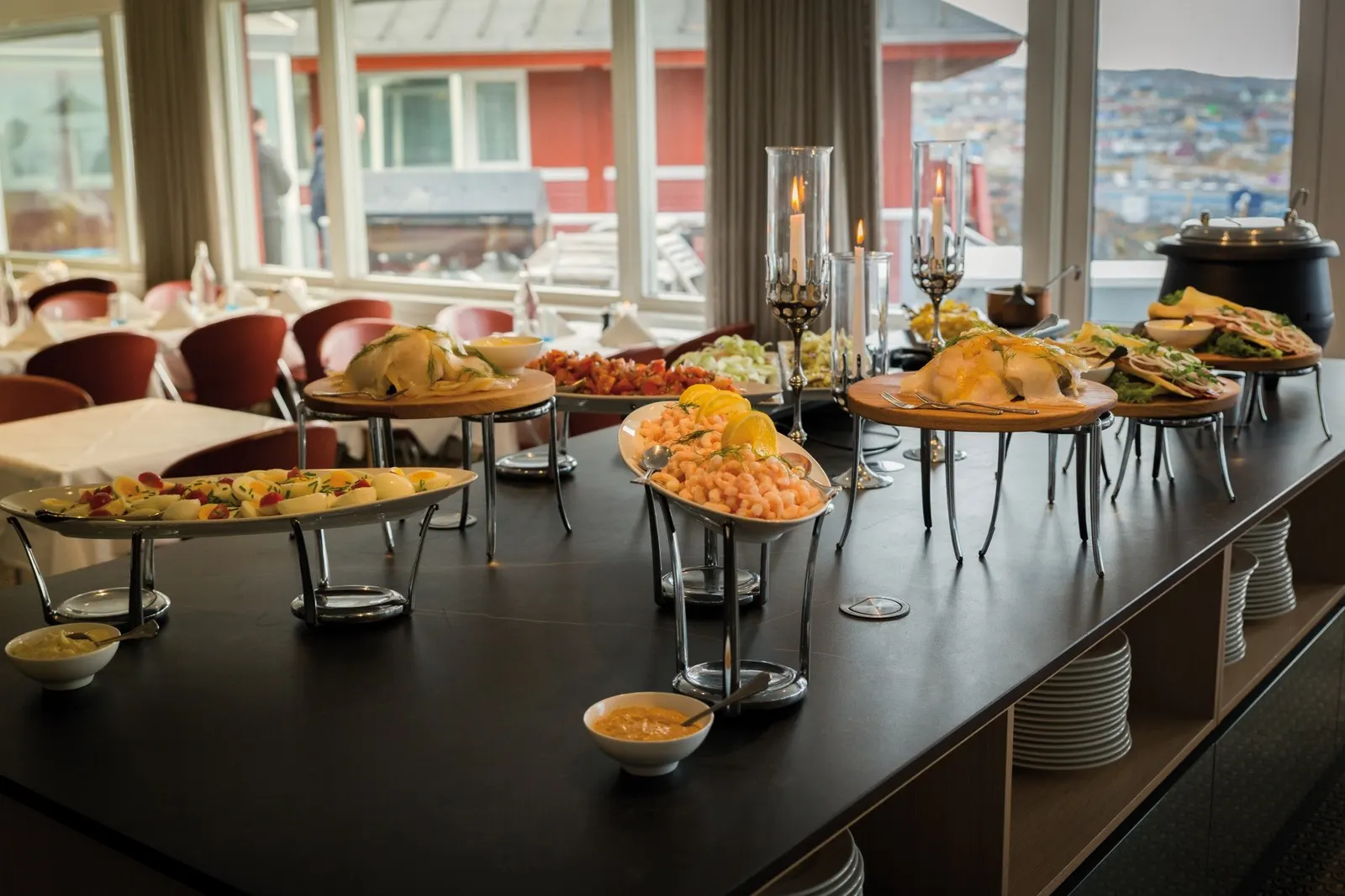 Buffetzeile mit Platten und Kerzenleuchtern, dahinter rote Holzhäuser in Grönland
