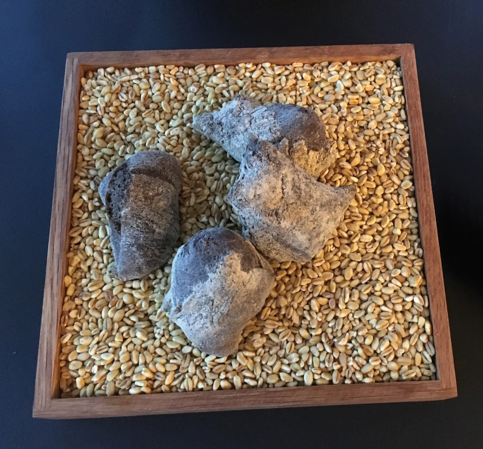 Vier rustikale Brotstücke auf einem Holztablett mit Weizenkörnern im Restaurant Ulo