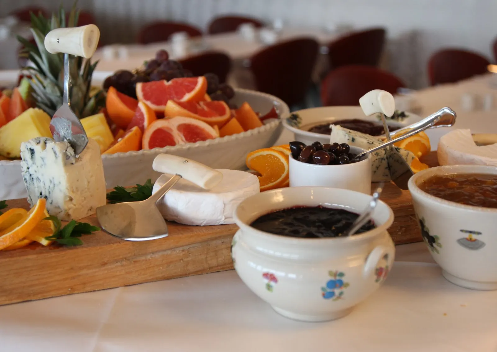 Käseplatte mit Blauschimmel, Brie, Grapefruit und Marmeladenschalen auf weißer Tischdecke