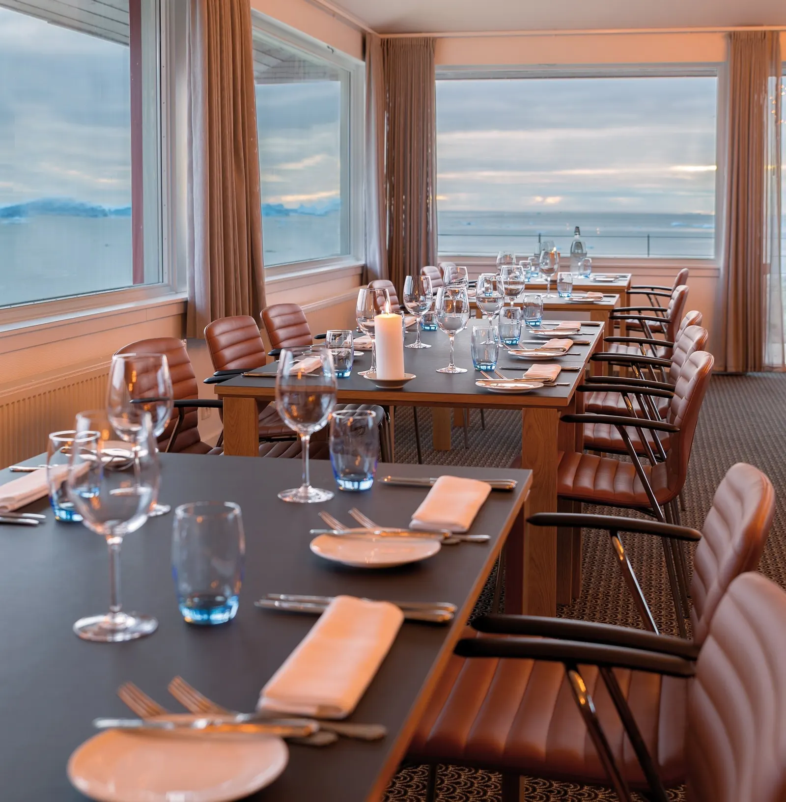 Lange gedeckte Tische im Eckfenster des Restaurant Ulo mit Blick auf Meer und Berge