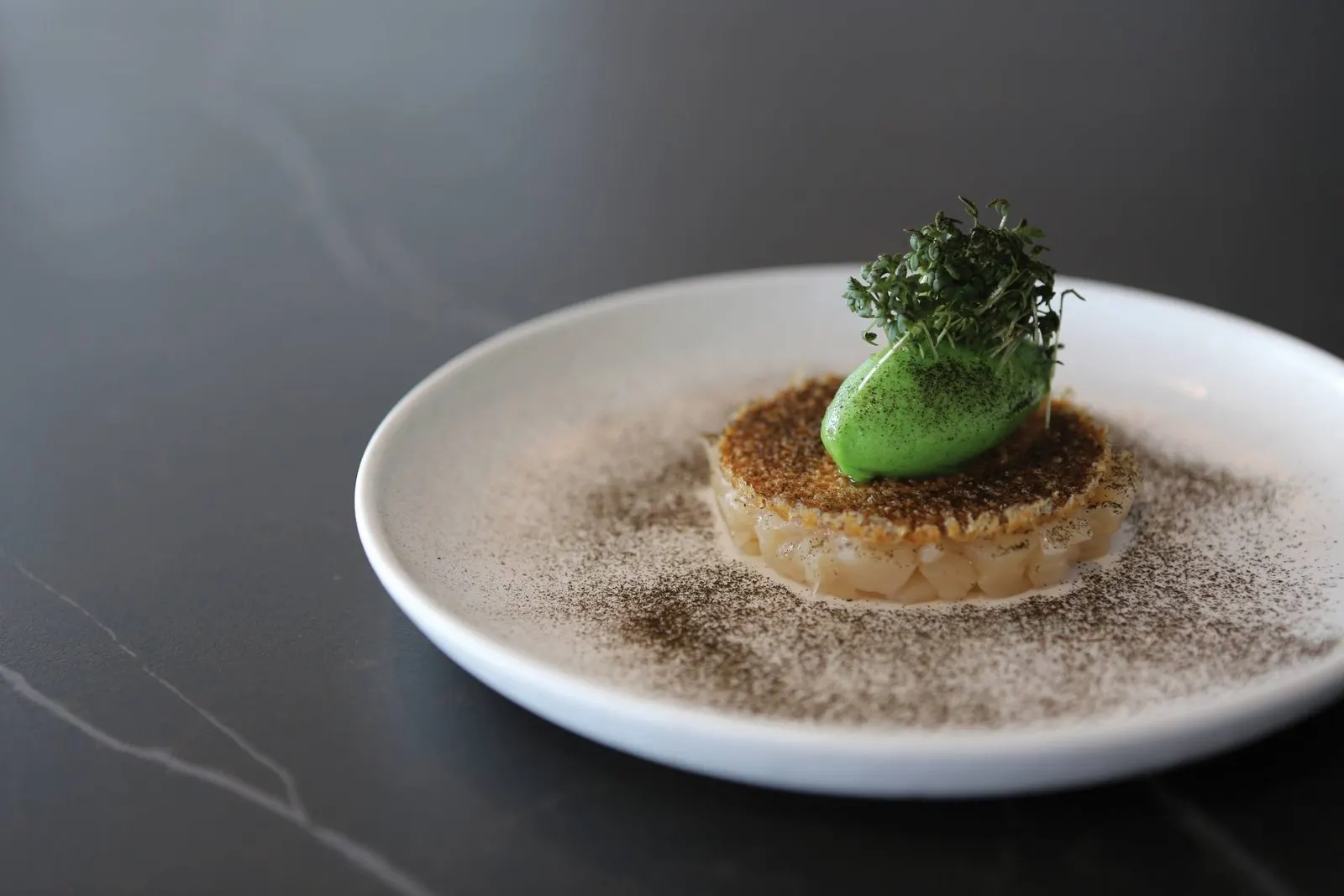 Gratinierte Kammmuschel mit grüner Kräutercreme und Kresse auf weißem Teller im Restaurant Ulo