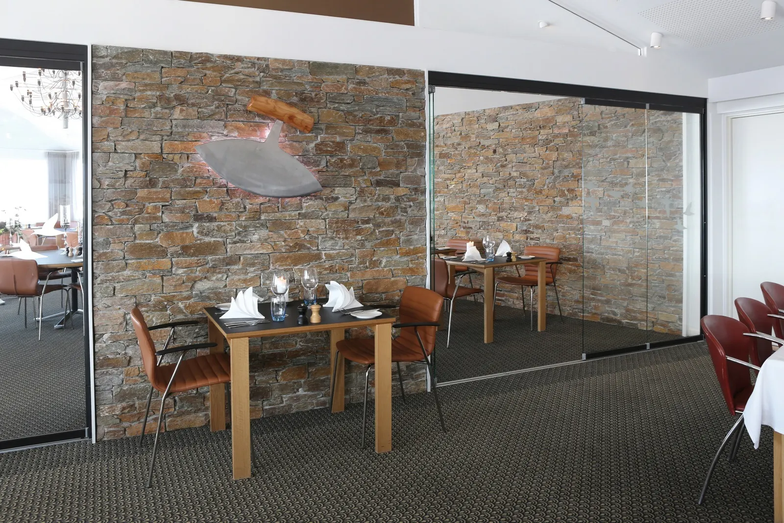 Gastraum des Restaurant Ulo mit Natursteinwand und Ulu-Messer als Wandobjekt