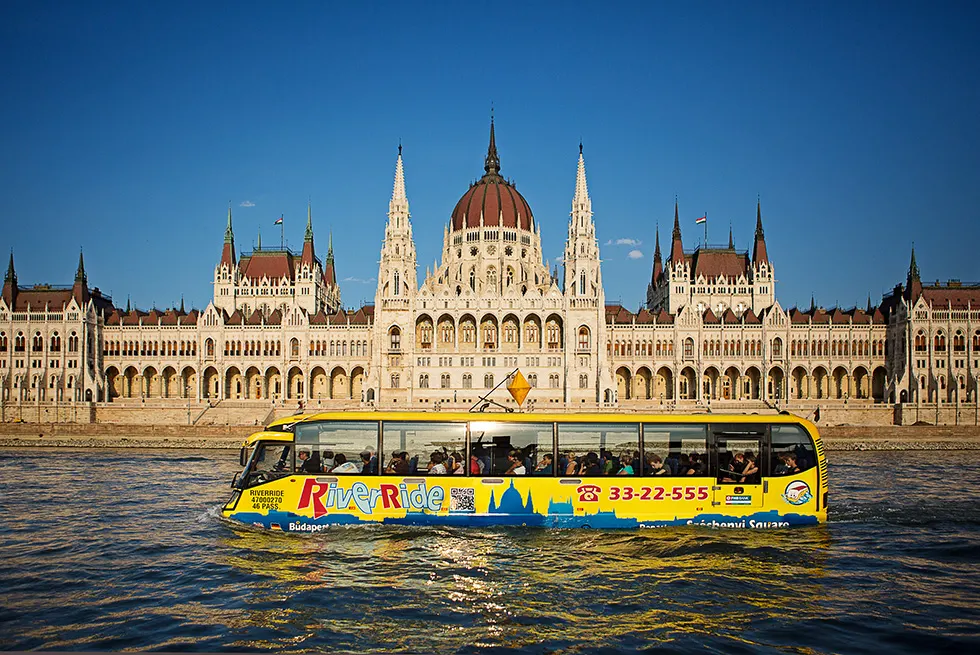 Gelb-blauer RiverRide-Amphibienbus mit Fahrgästen auf der Donau vor dem Parlamentsgebäude in Budapest