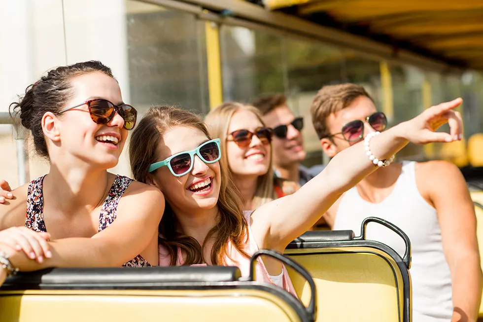Lachende junge Leute auf dem Oberdeck eines gelben Sightseeing-Busses