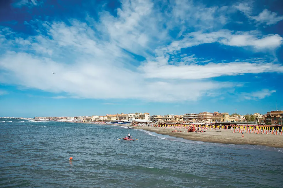 Sandstrand mit Reihen bunter Sonnenschirme und Häuserzeile am Meer unter Wolkenhimmel