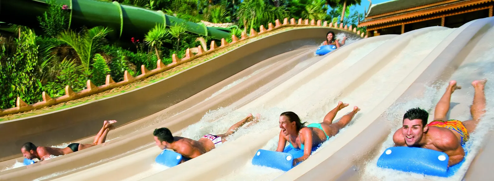 Badegäste rutschen auf Matten kopfvoran die breite weiße Mattenrutsche im Siam Park hinab