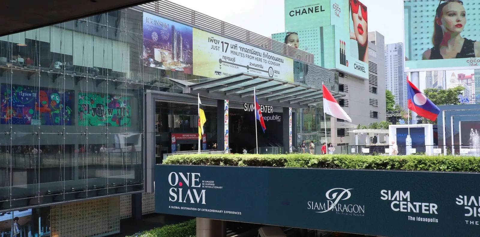 Eingang des Siam Center mit Werbetafeln, Flaggen und den Schriftzügen One Siam und Siam Paragon