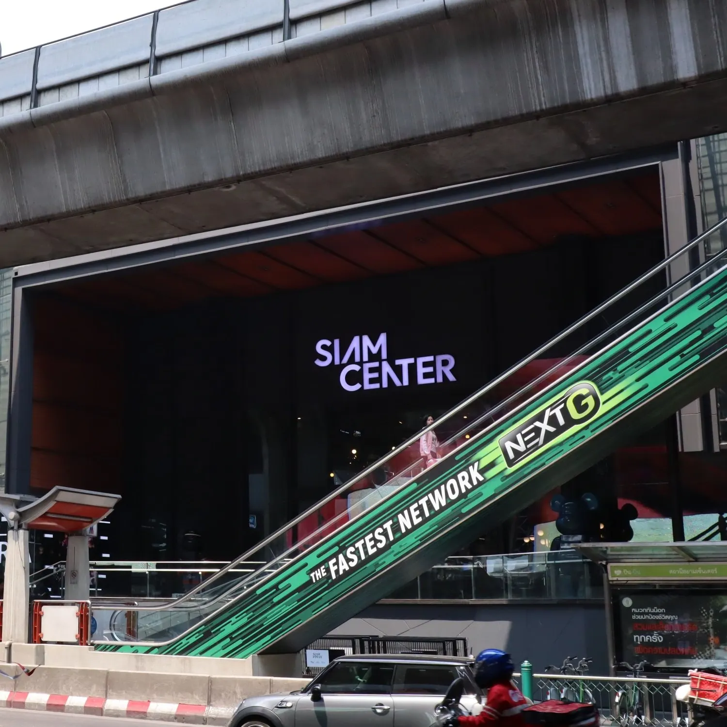 Rolltreppe zum Siam Center unter der Hochbahntrasse, davor Straßenverkehr