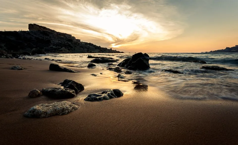 Sandstrand mit nassen Steinen und auslaufenden Wellen im Abendlicht