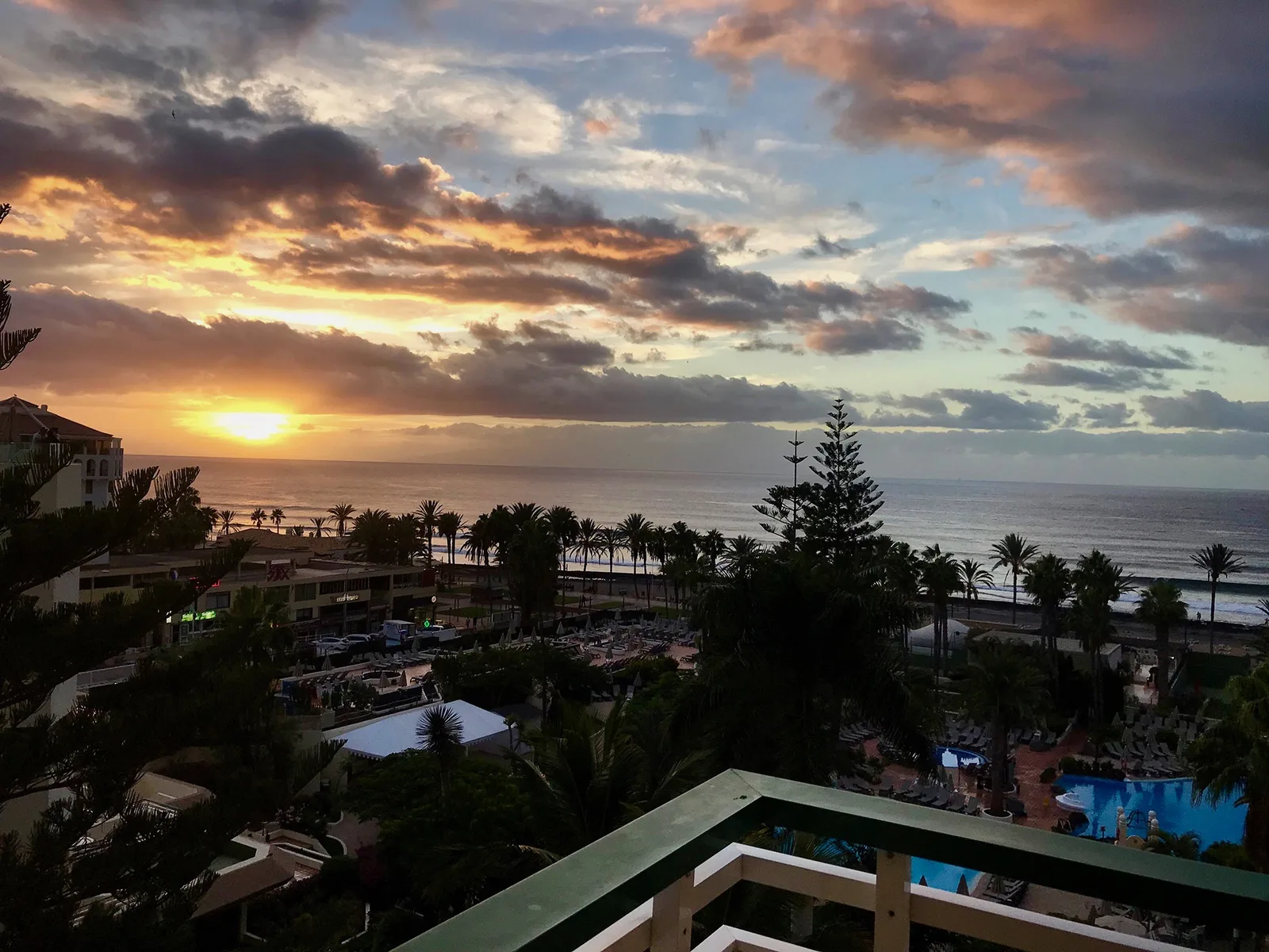 Sonnenuntergang über dem Meer mit Palmen, Hotelpools und der Promenade von Playa de las Américas
