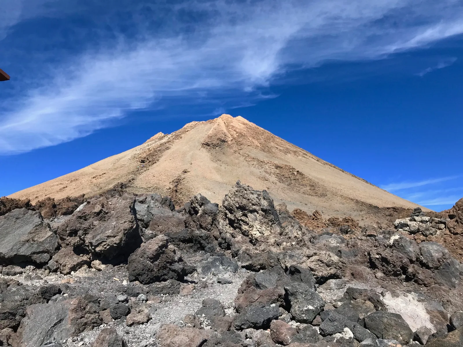 Gipfelkegel des Teide über dunklem Lavagestein unter blauem Himmel