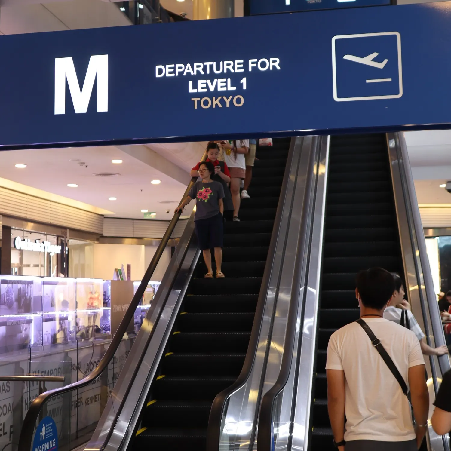 Rolltreppen unter einem Flughafenschild mit der Aufschrift Departure for Level 1 Tokyo