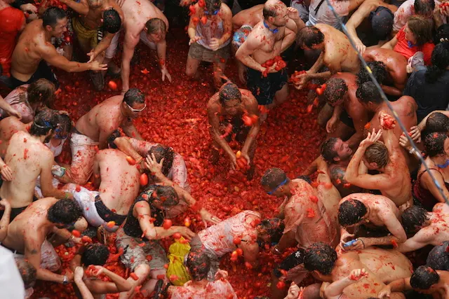 Menschenmenge wirft Tomaten in einer Straße, alle sind rot bespritzt