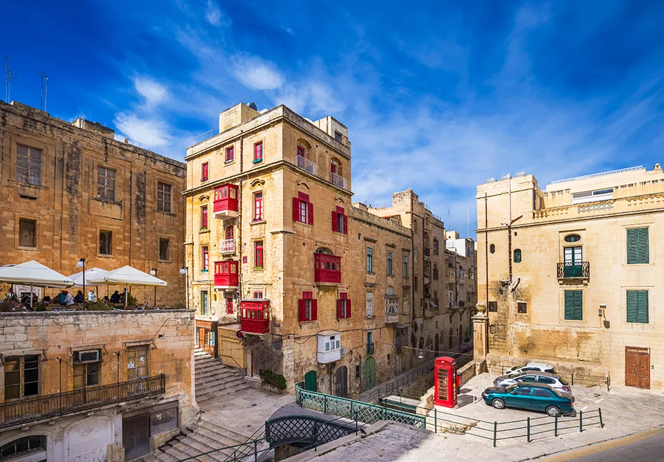 Kalksteinhäuser mit roten Holzbalkonen und eine rote Telefonzelle an einem Platz in Valletta
