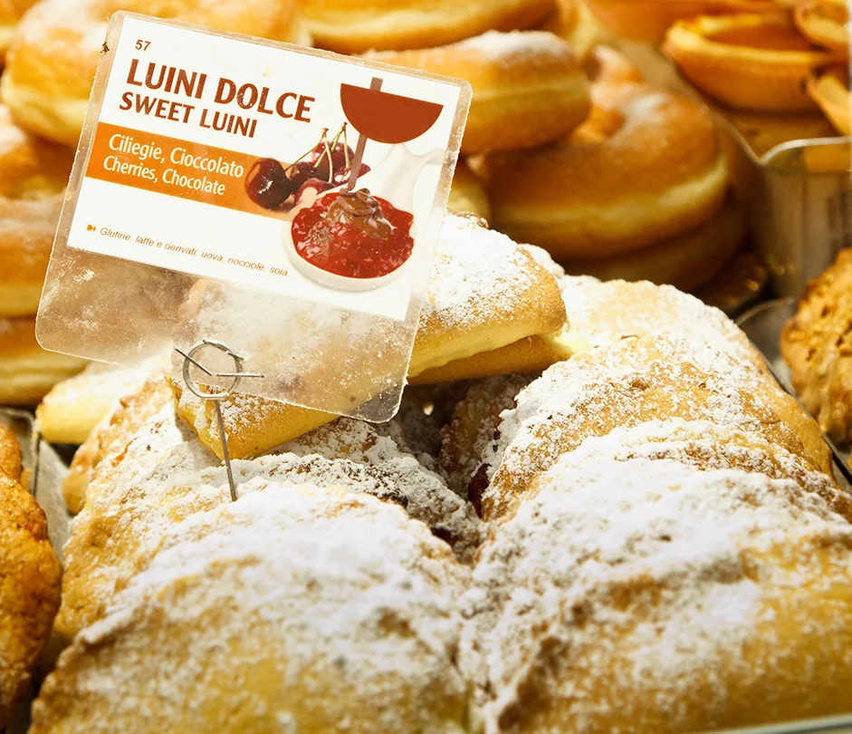 Mit Puderzucker bestäubte süße Panzerotti in der Auslage, davor ein Schild Luini Dolce